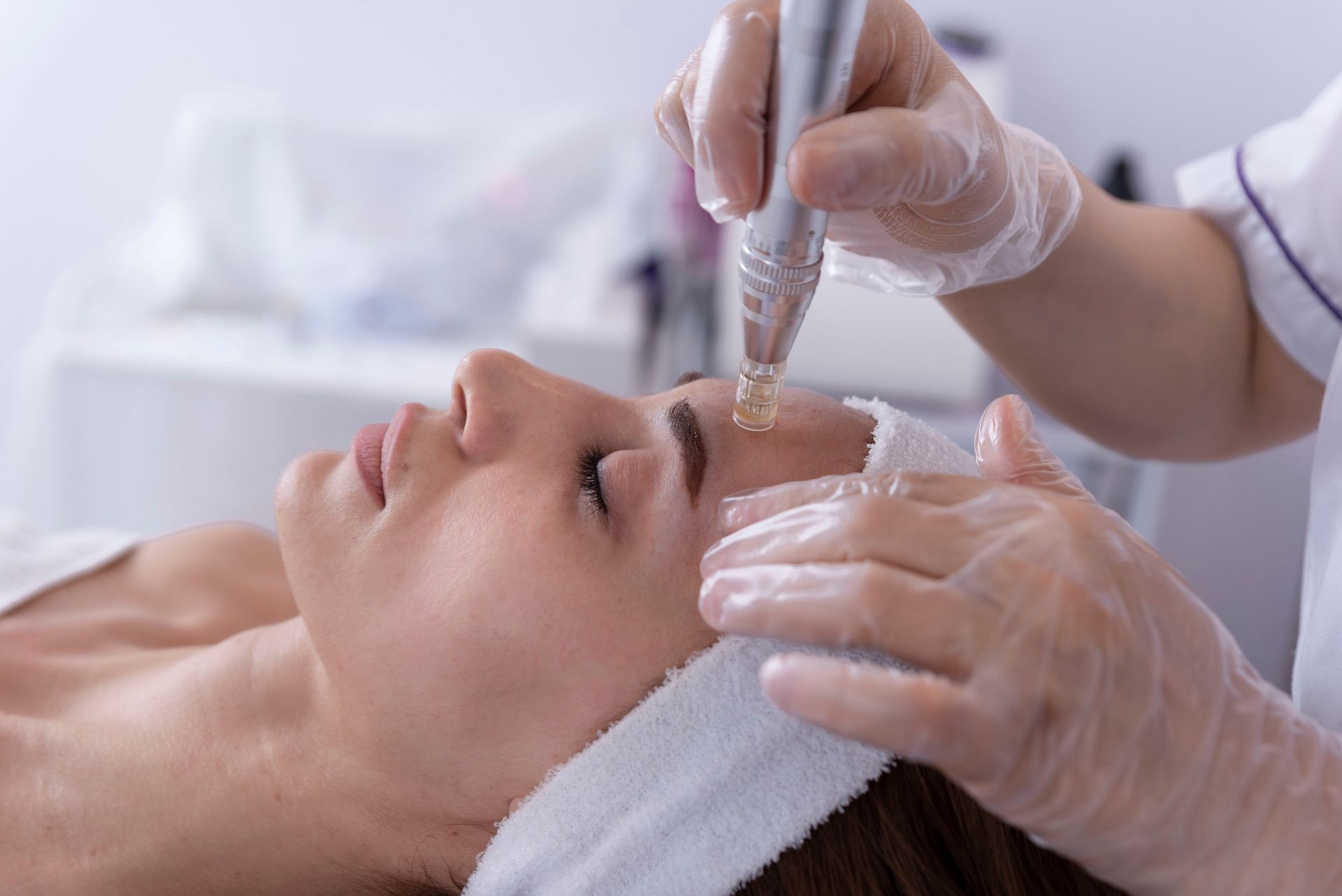 Des mains gantées appliquent un sérum de soin sur le visage d'une femme lors d'un soin esthétique.