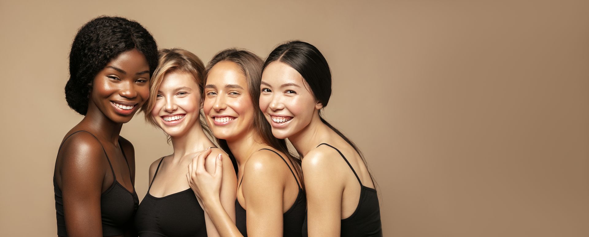 Quatre amis souriants, vêtus de hauts noirs, posent ensemble sur un fond beige.