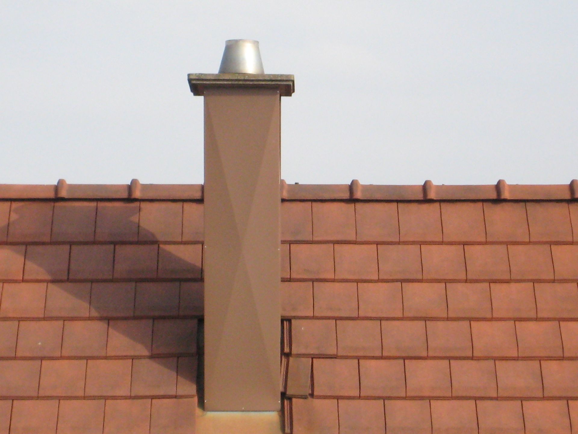 Cheminée brune sur un toit de tuiles brun-rougeâtre.