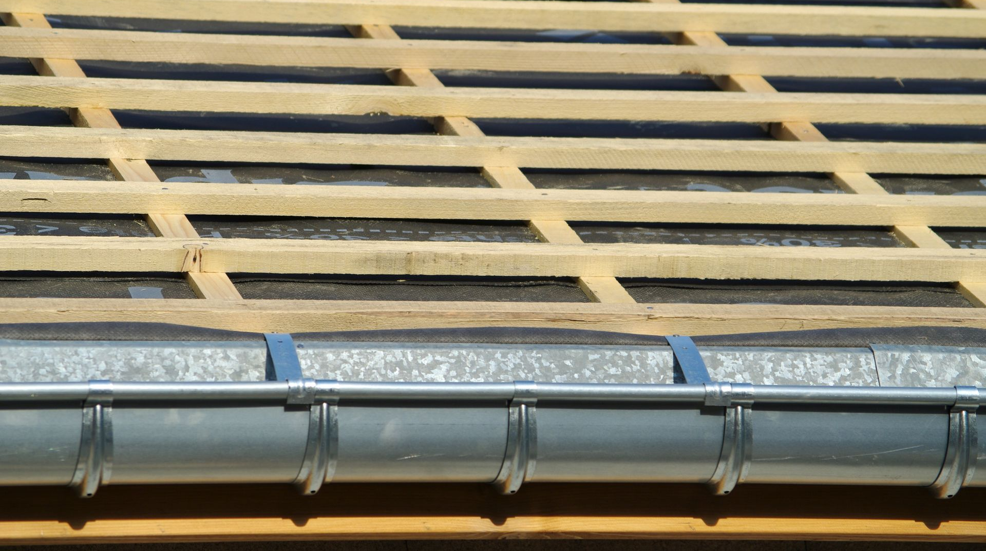 Toiture en construction avec chevrons en bois et gouttière grise.