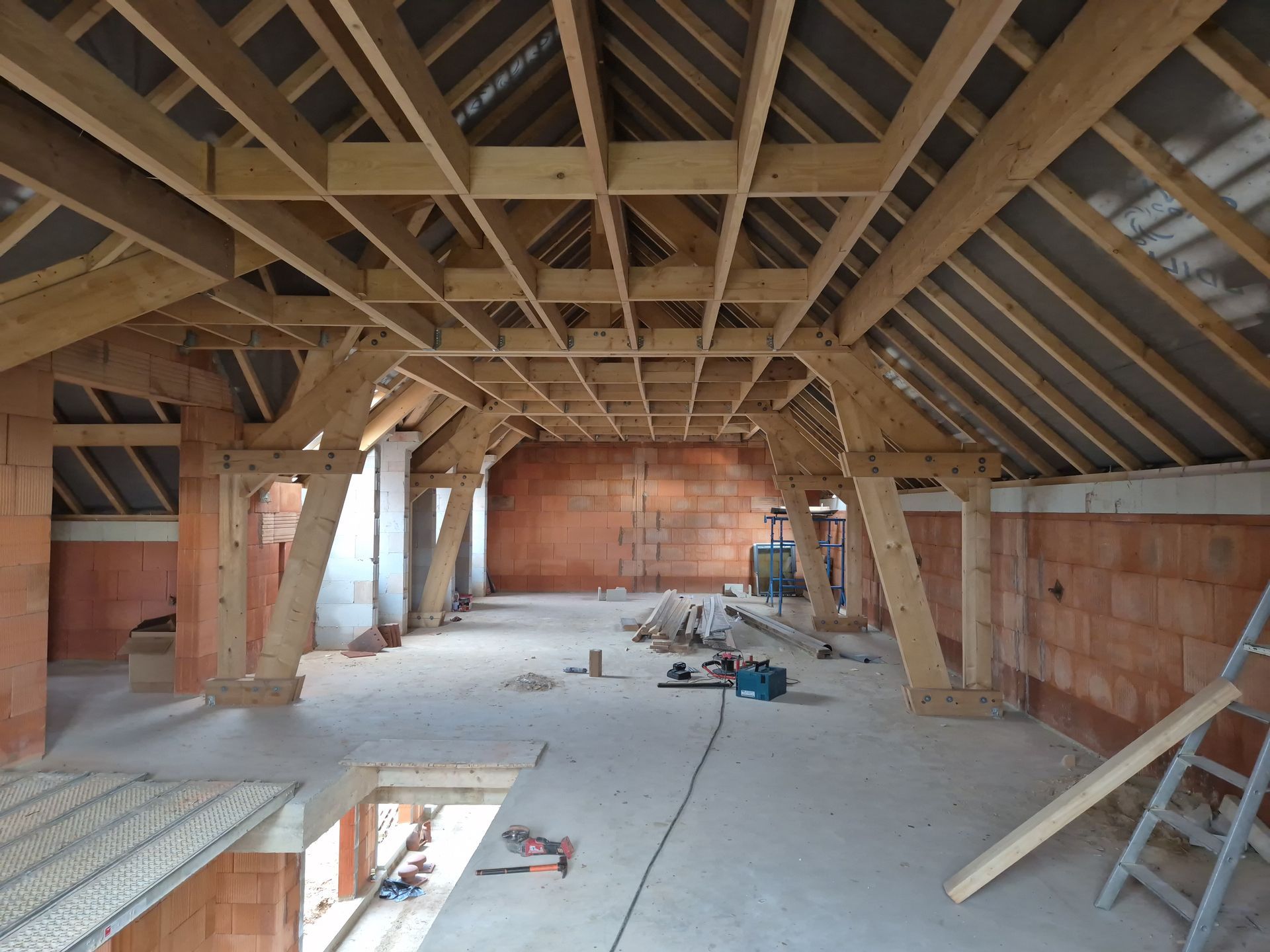 Intérieur d'un grenier non aménagé avec poutres en bois apparentes, murs en briques et matériaux de construction.