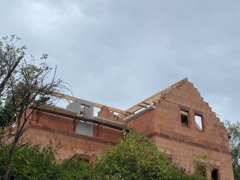 Maison en briques en construction, toiture inachevée, sur fond de ciel nuageux.