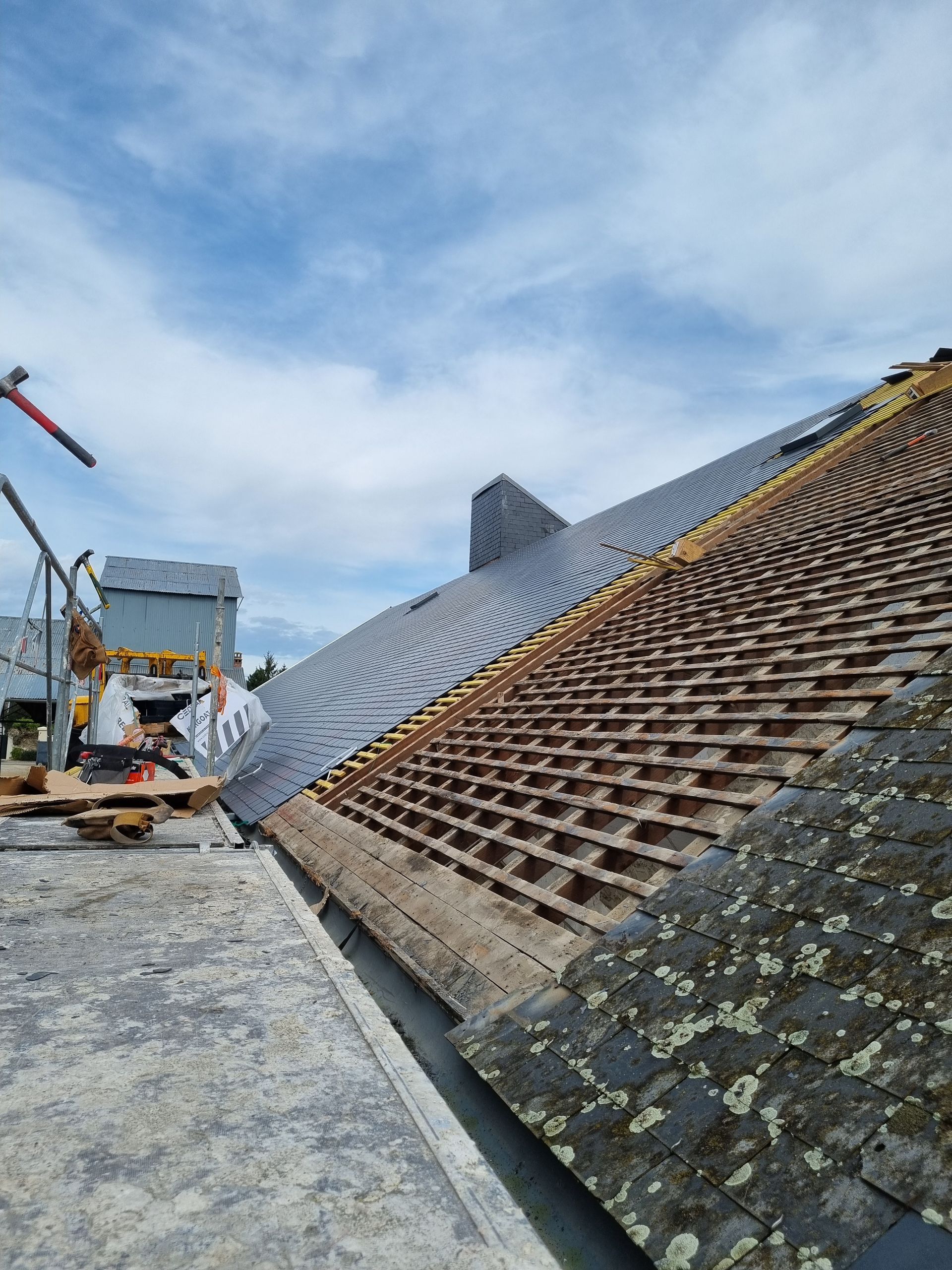 Toiture partiellement dénudée de tuiles, révélant une sous-toiture en bois, sur un bâtiment en construction.