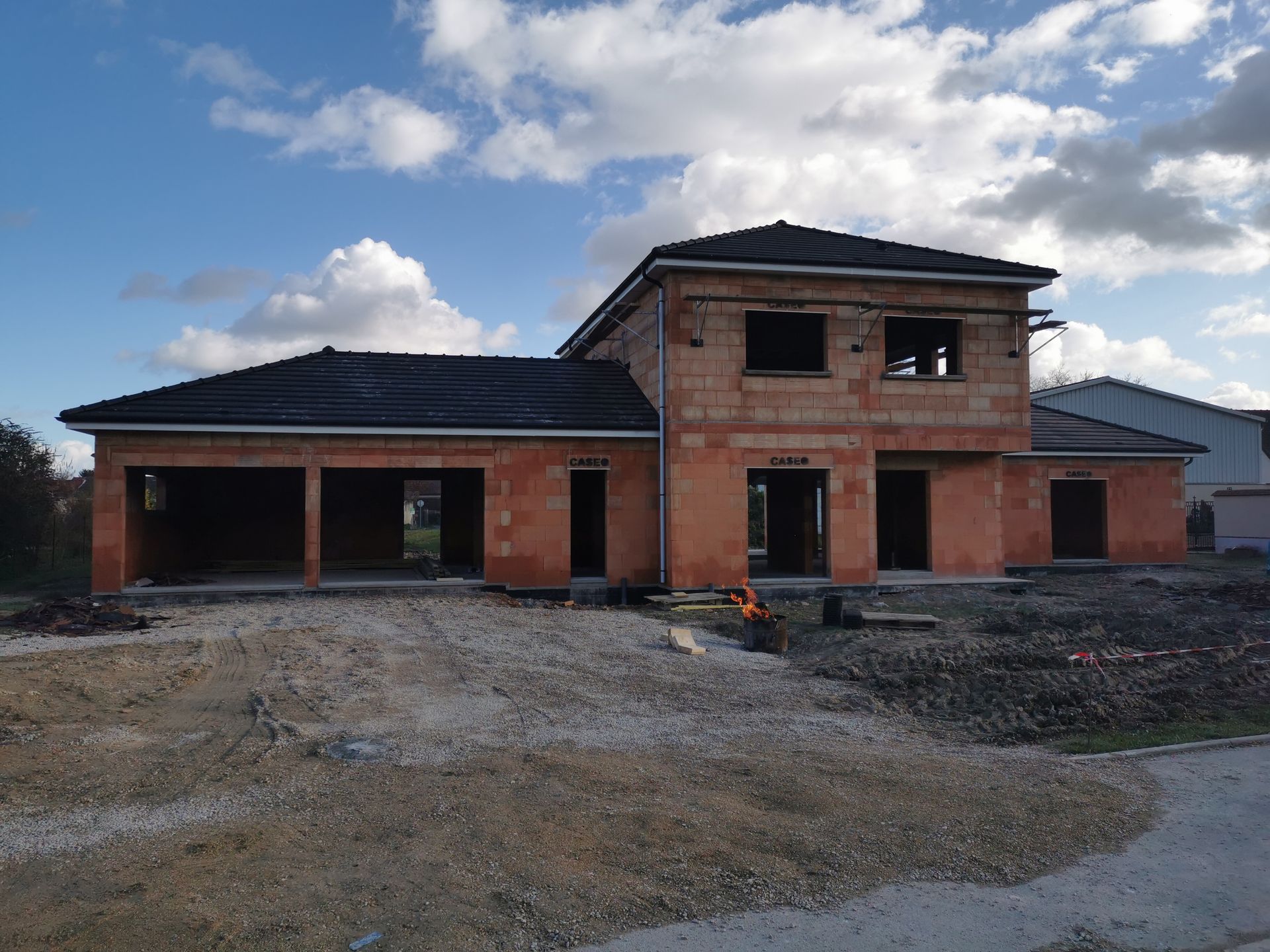 Chantier : maison en briques rouges avec garage attenant sous un ciel bleu.