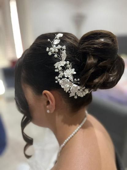 Donna con i capelli scuri raccolti in uno chignon, che indossa una collana di perle e una parrucca floreale.