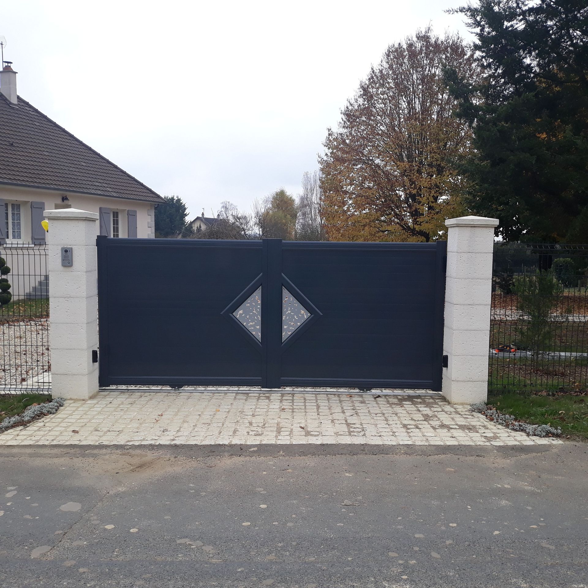 Portail d'allée en métal noir entre des piliers en pierre blanche devant une maison