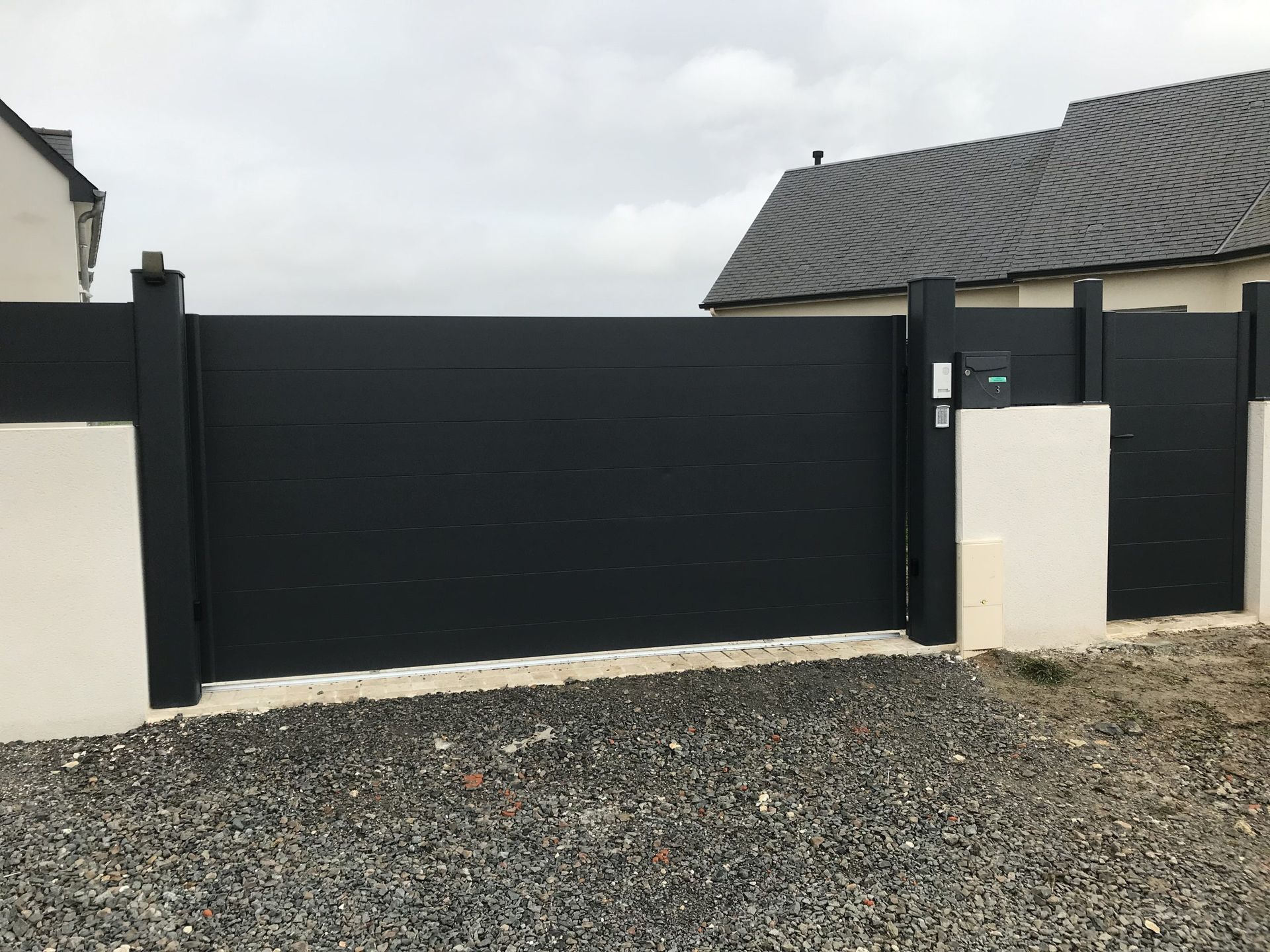Portail d'allée noir avec piliers blancs et allée de gravier devant une maison