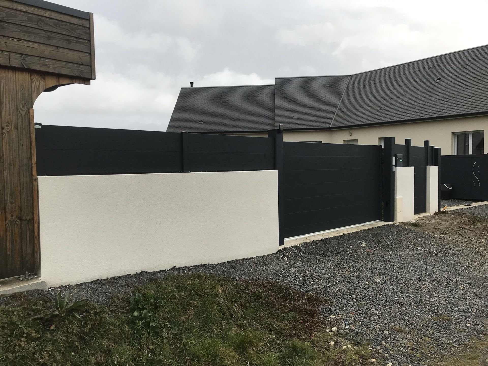 Maison blanche moderne avec clôture noire et allée de gravier sous un ciel nuageux