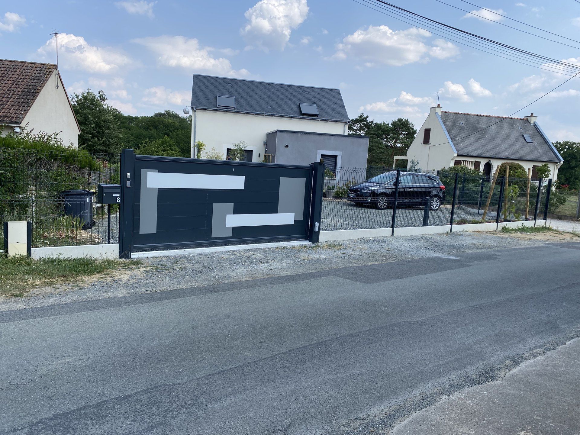 Rue résidentielle avec des maisons blanches et une clôture bleu foncé au bord d'une route sous un ciel nuageux