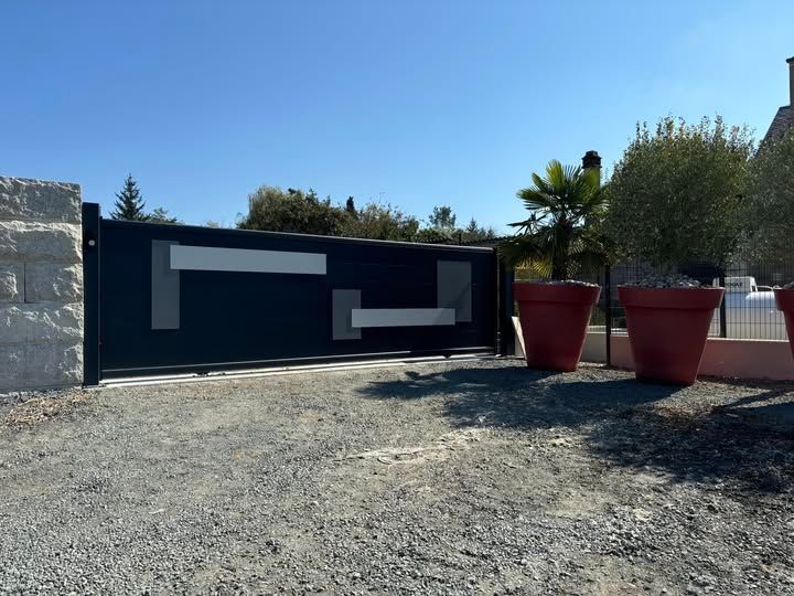 Mur moderne noir et blanc avec jardinières rouges sur une terrasse en gravier sous un ciel bleu