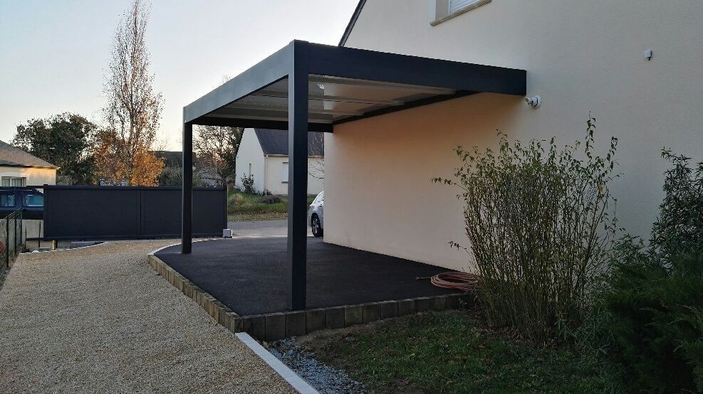 Patio d'une maison moderne avec une pergola noire, un chemin de gravier et des arbustes le long d'un mur blanc.