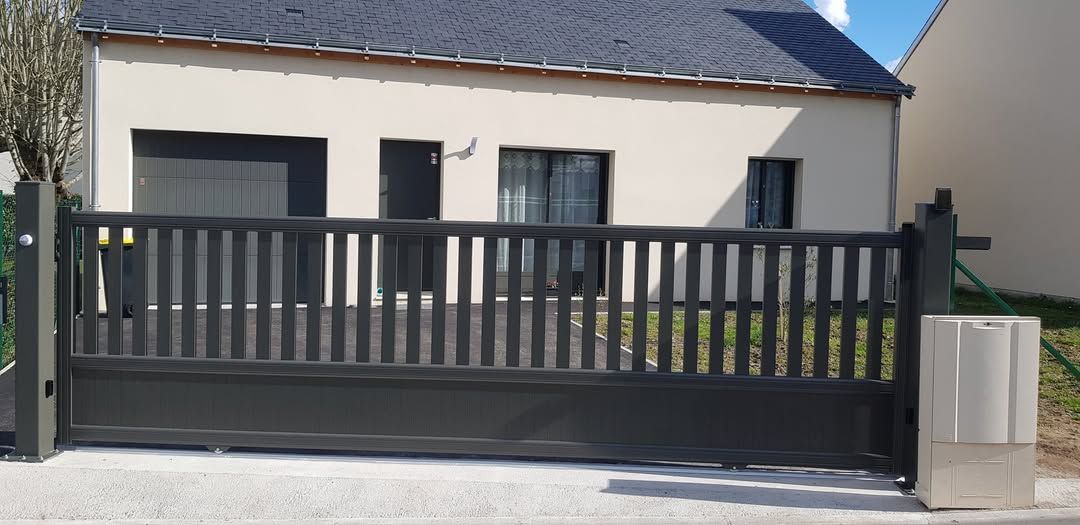 Maison moderne avec portail et clôture gris foncé devant une allée.