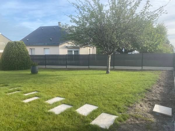 Pelouse arrière avec pas japonais, un arbre et une clôture sombre devant une maison