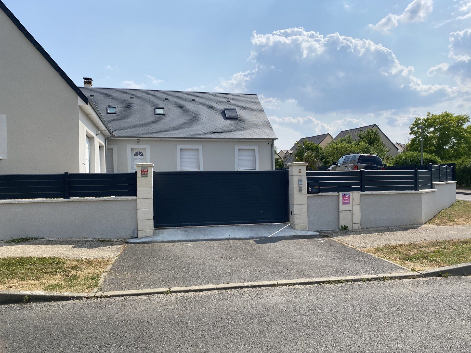 Maison d'habitation avec portail et clôture bleus, vue de la rue sous un ciel partiellement nuageux