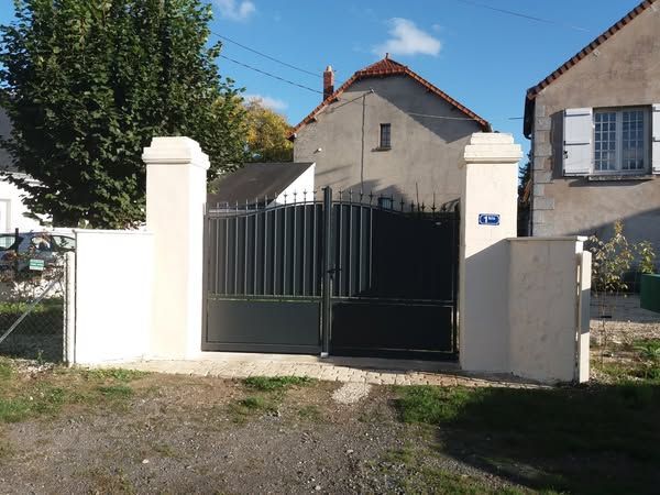 Portail vert fermé entre des piliers blancs devant une maison par une journée ensoleillée