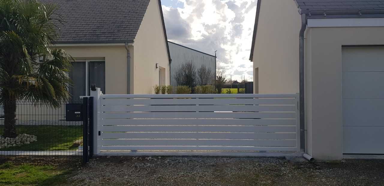Portail coulissant blanc moderne entre deux maisons, avec garage sur la droite.