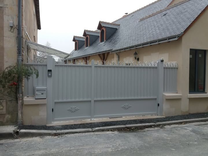 Portail métallique gris devant un bâtiment beige dans une rue étroite