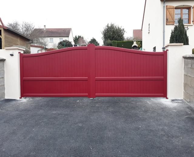 Portail rouge entre des murs blancs à l'entrée d'une propriété résidentielle.