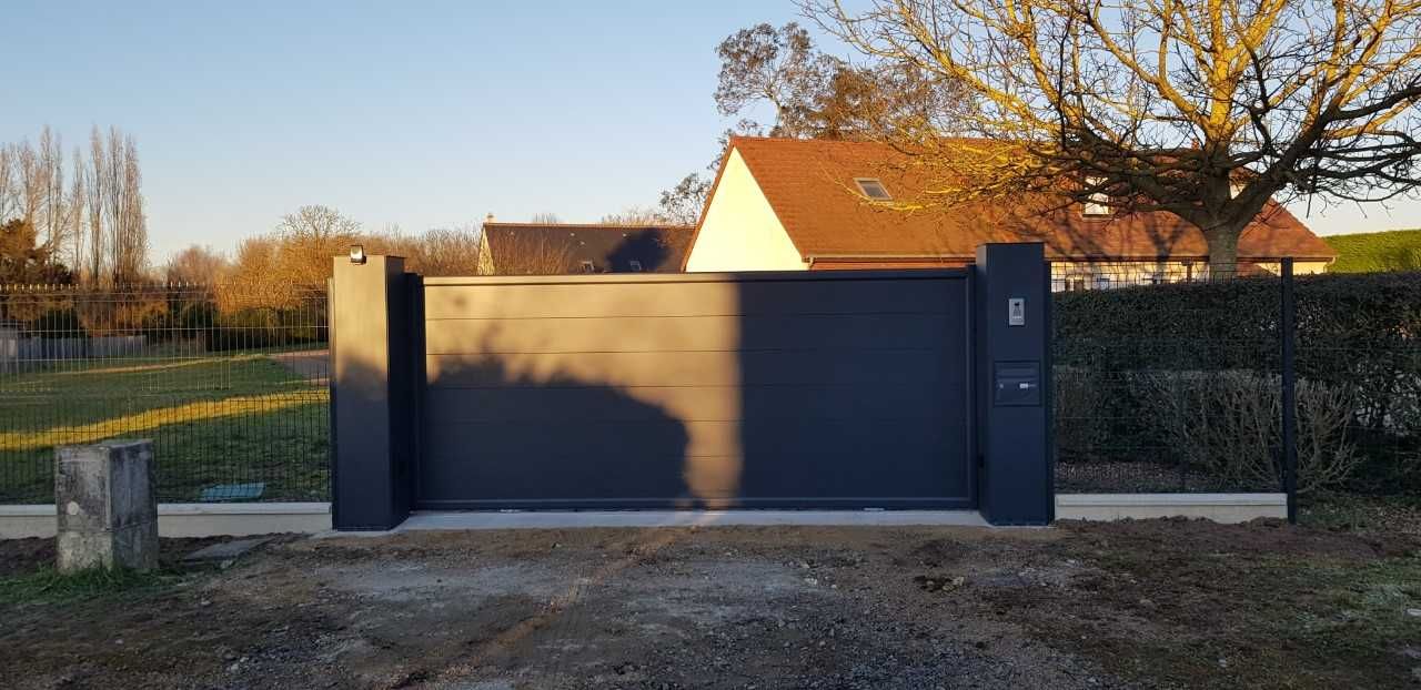 Portail bleu foncé fermé devant une maison au coucher du soleil