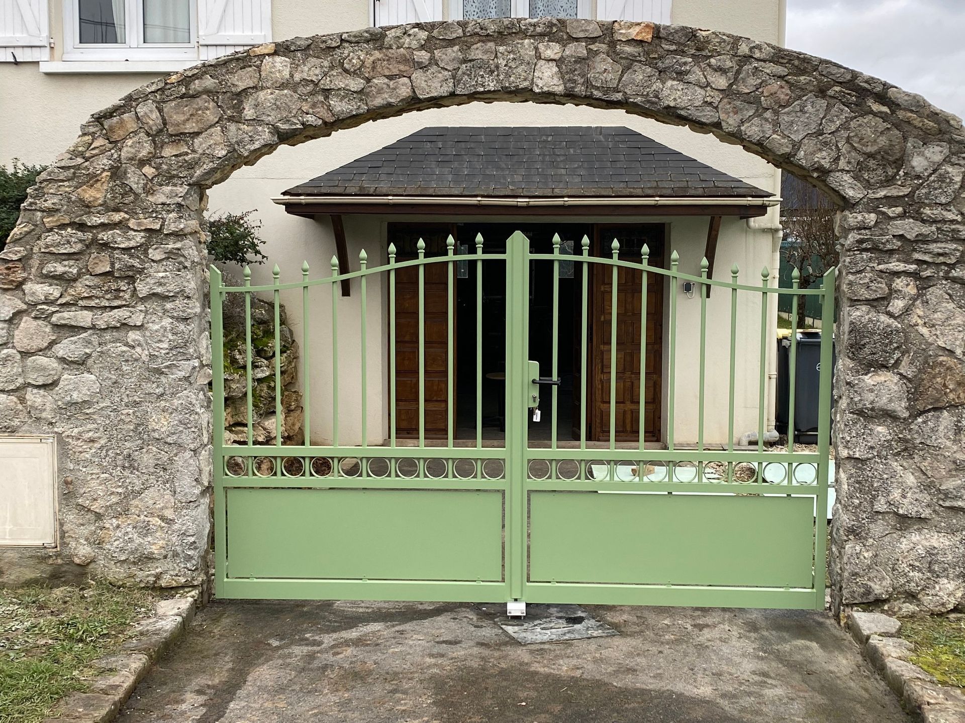Portail en métal vert encastré dans une arche en pierre à l'entrée d'une maison