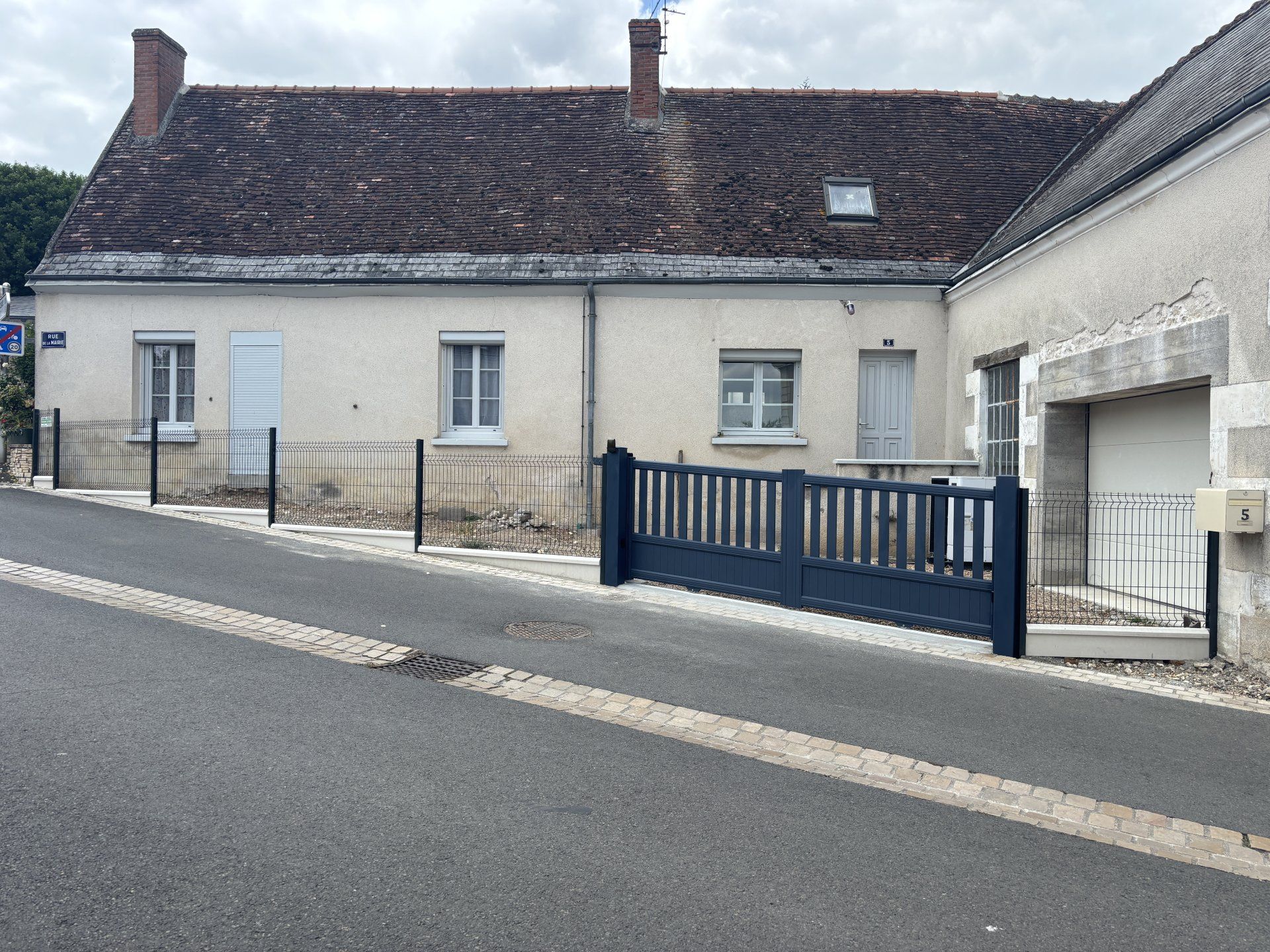 Rangée de petites maisons en pierre avec une clôture bleue le long d'une rue en pente