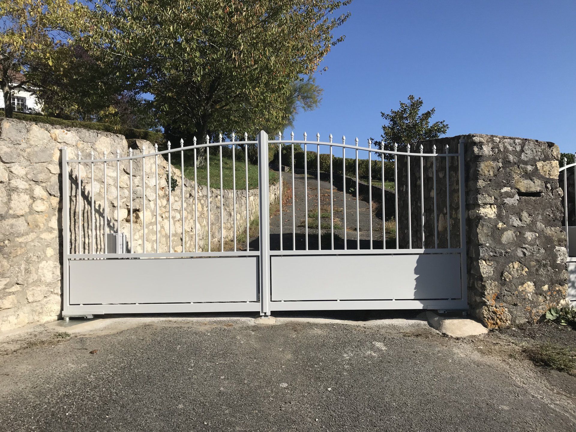 Portail métallique gris fermé entre des murs en pierre à l'entrée d'une allée