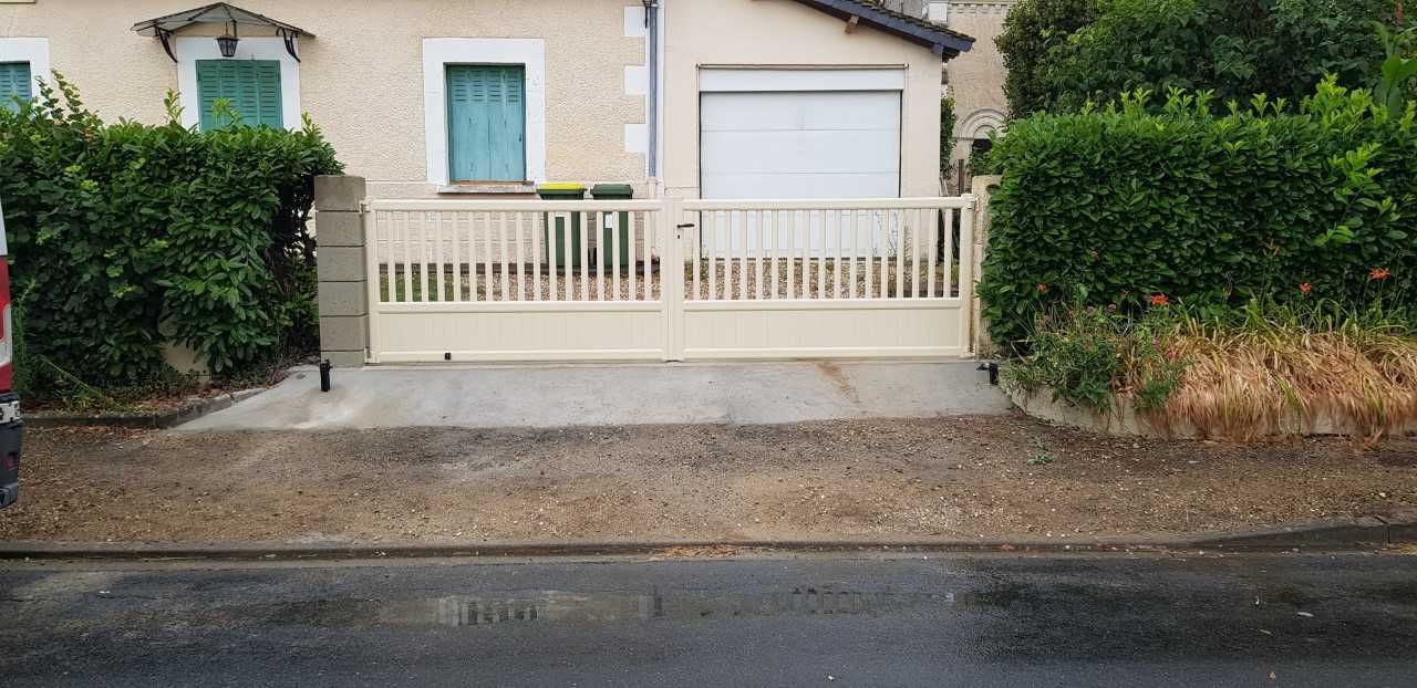 Petite maison beige avec une balustrade blanche, des volets verts, des haies et une route mouillée en bordure de route.