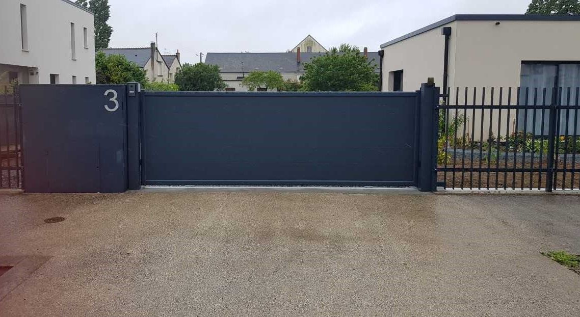 Portail d'entrée bleu foncé avec clôture et allée de gravier devant les maisons