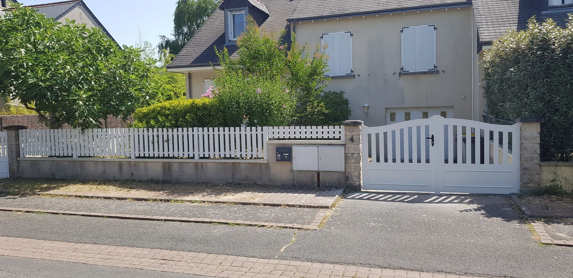 Maison blanche avec cour avant clôturée et portail d'entrée au bord d'une route en plein jour