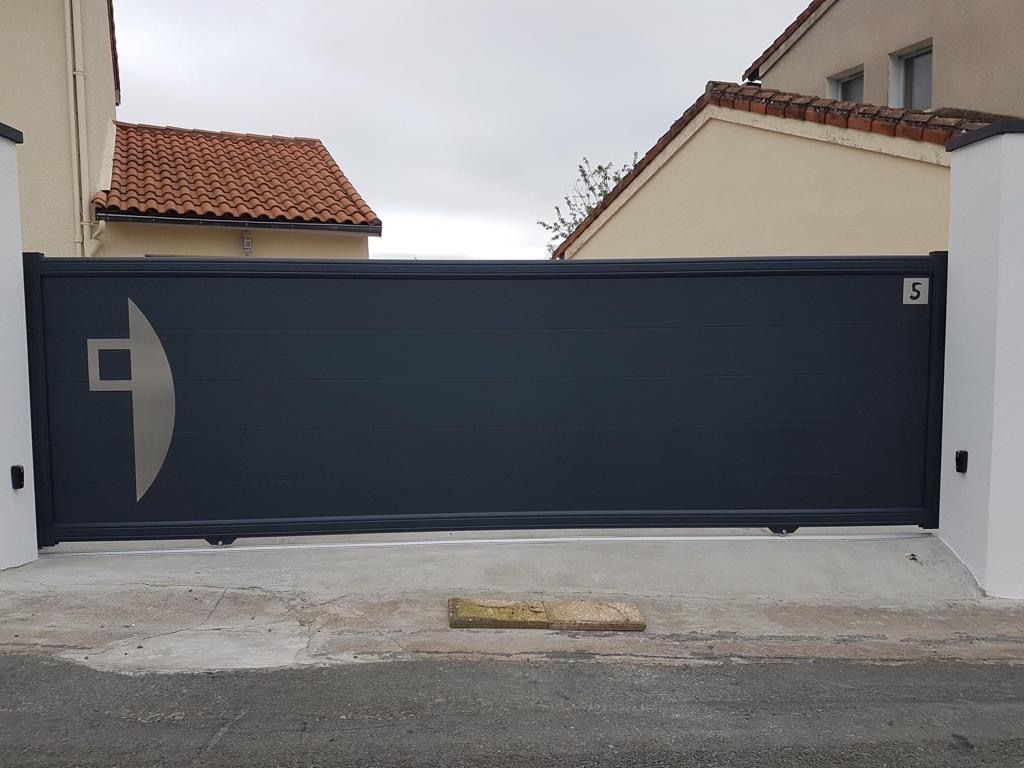 Portail de garage coulissant gris foncé à motif géométrique, installé dans une allée résidentielle.