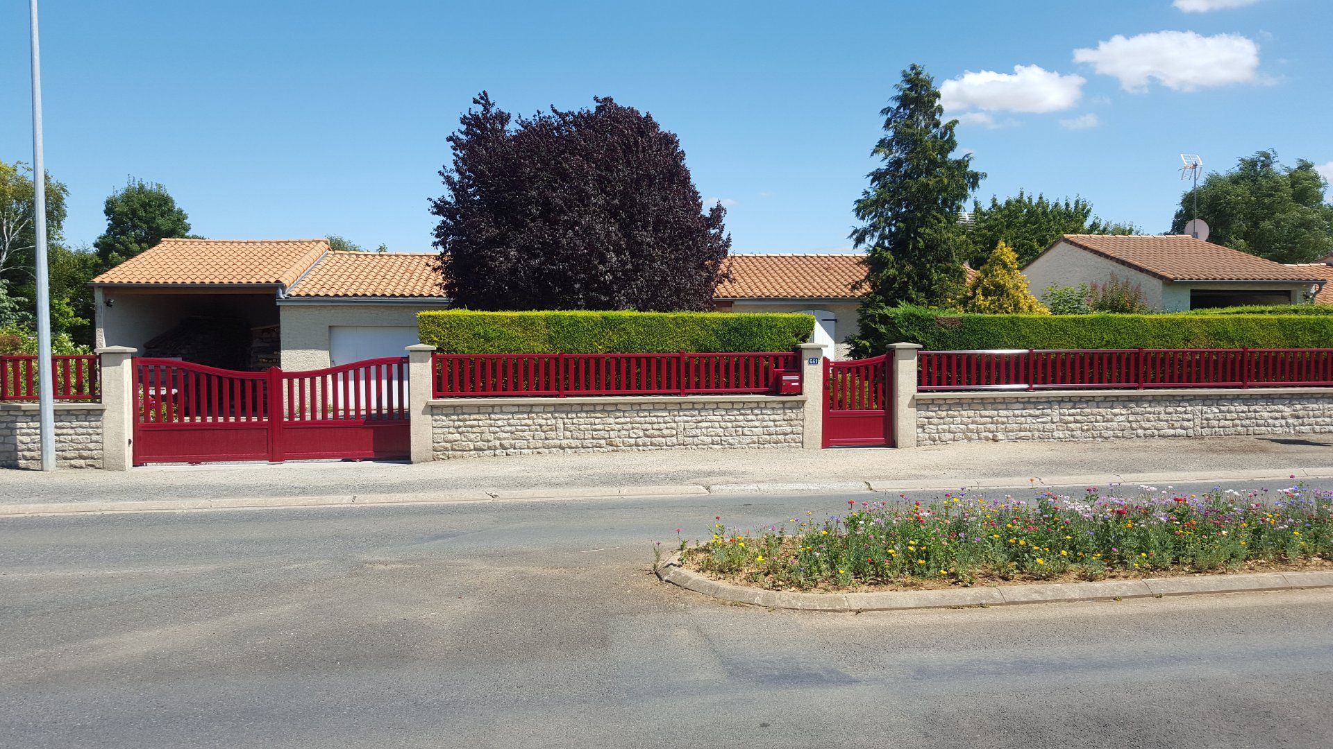 Maison de plain-pied avec clôture et portail rouges, arbres devant, vue depuis une rue calme