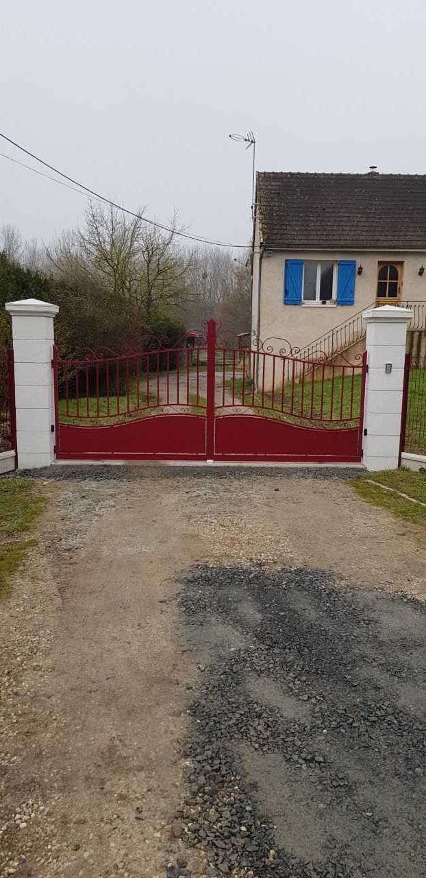 Portail rouge entre des piliers blancs à l'entrée d'une maison de campagne sur un chemin de gravier