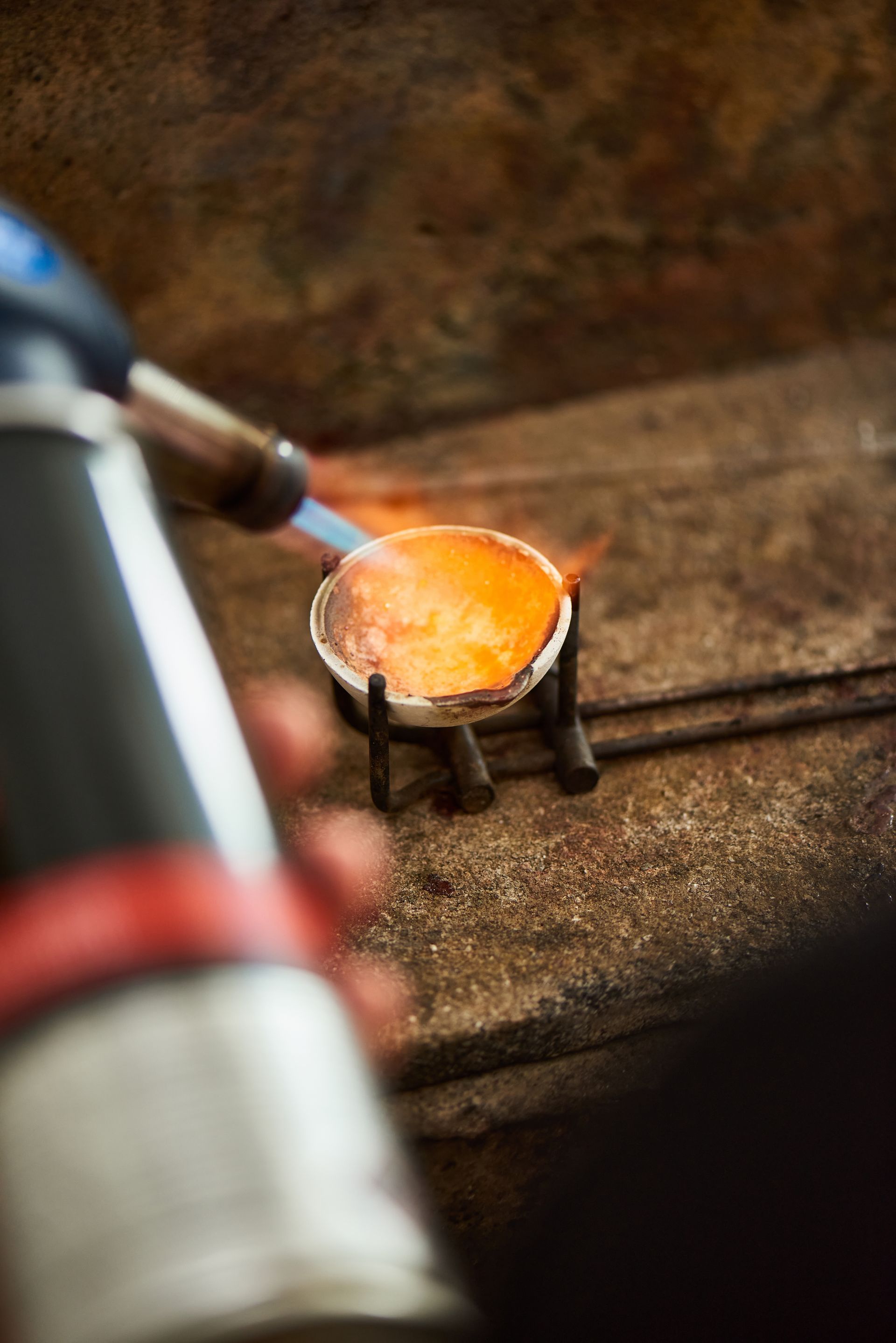 De l'or en fusion dans un creuset, chauffé par une torche bleu et noir, sur une surface texturée.