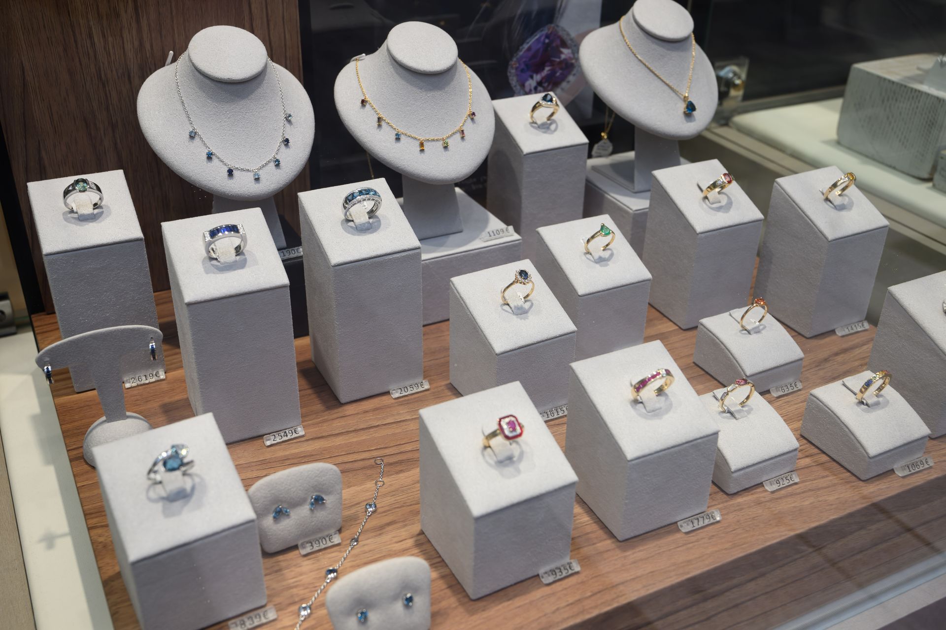 Vitrine à bijoux présentant colliers et bagues sur des socles blancs, disposés sur une surface en bois.