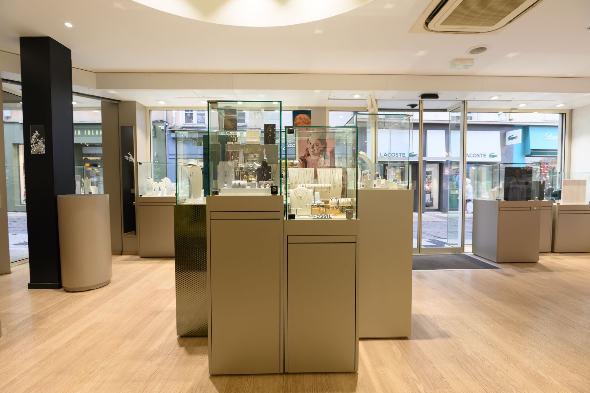 Intérieur d'une bijouterie avec vitrines sur piédestaux, parquet et portes automatiques donnant sur la rue.