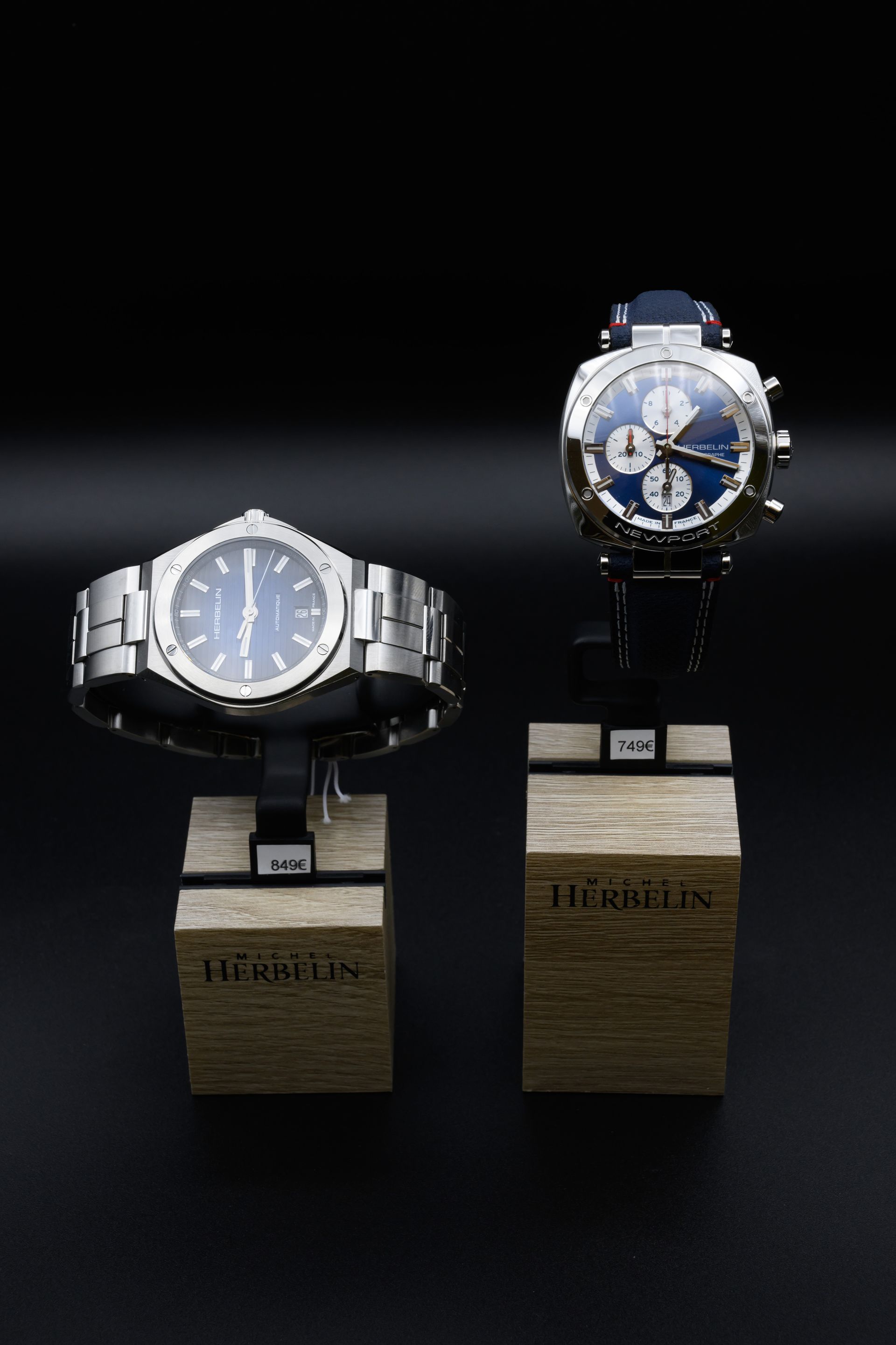 Deux montres-bracelets sur des présentoirs en bois, sur fond noir.