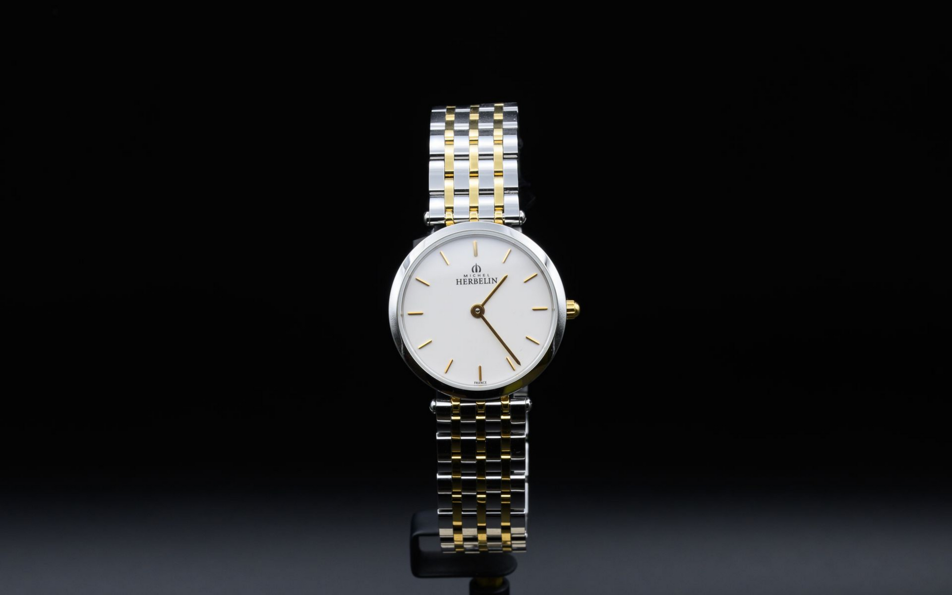 Montre-bracelet argentée et dorée sur une surface noire réfléchissante.