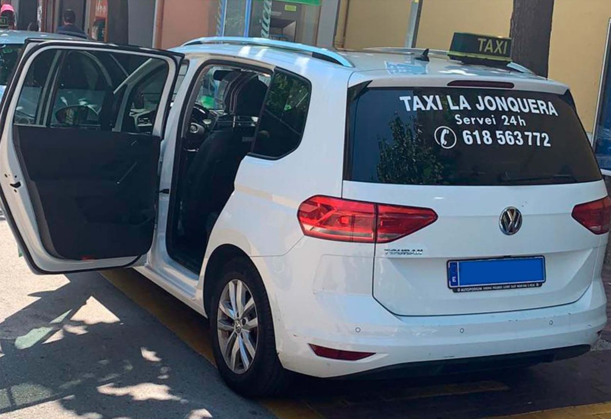 Un taxi blanco está estacionado al costado de la carretera con las puertas abiertas.