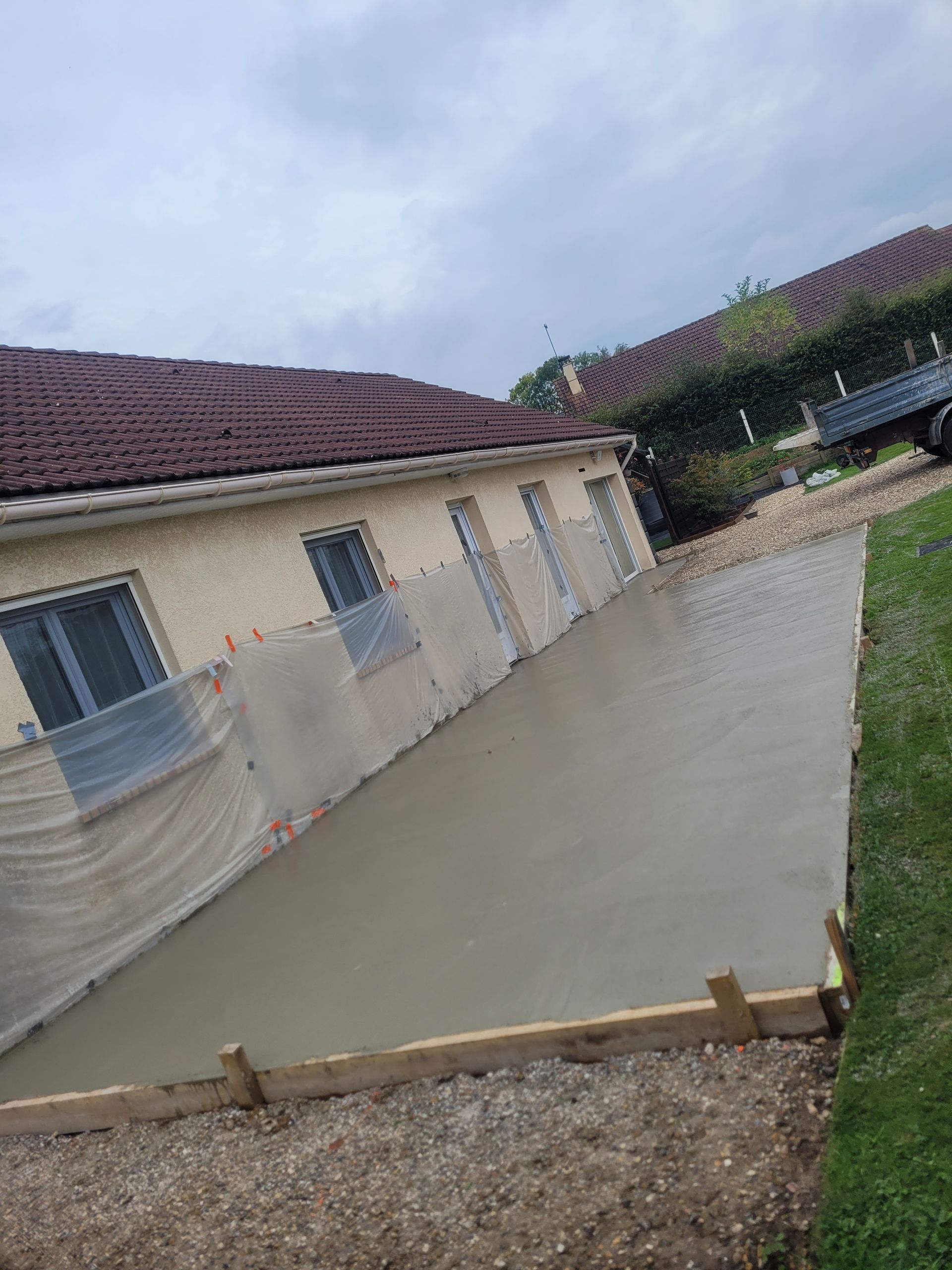 Maçonnerie terminée avant la mise en place d'un dallage de terrasse devant un pavillon protégé par des bâches