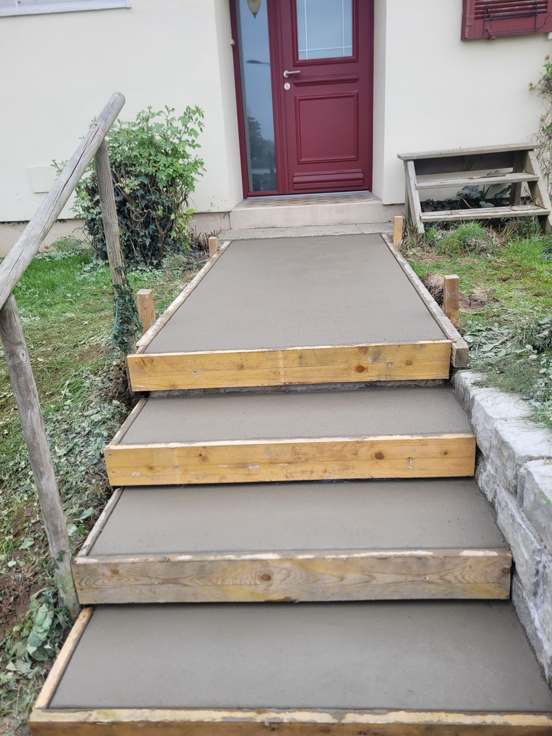 Travaux de maçonnerie en cours pour un escalier gris avec planches de bois sur les marches pour consolider
