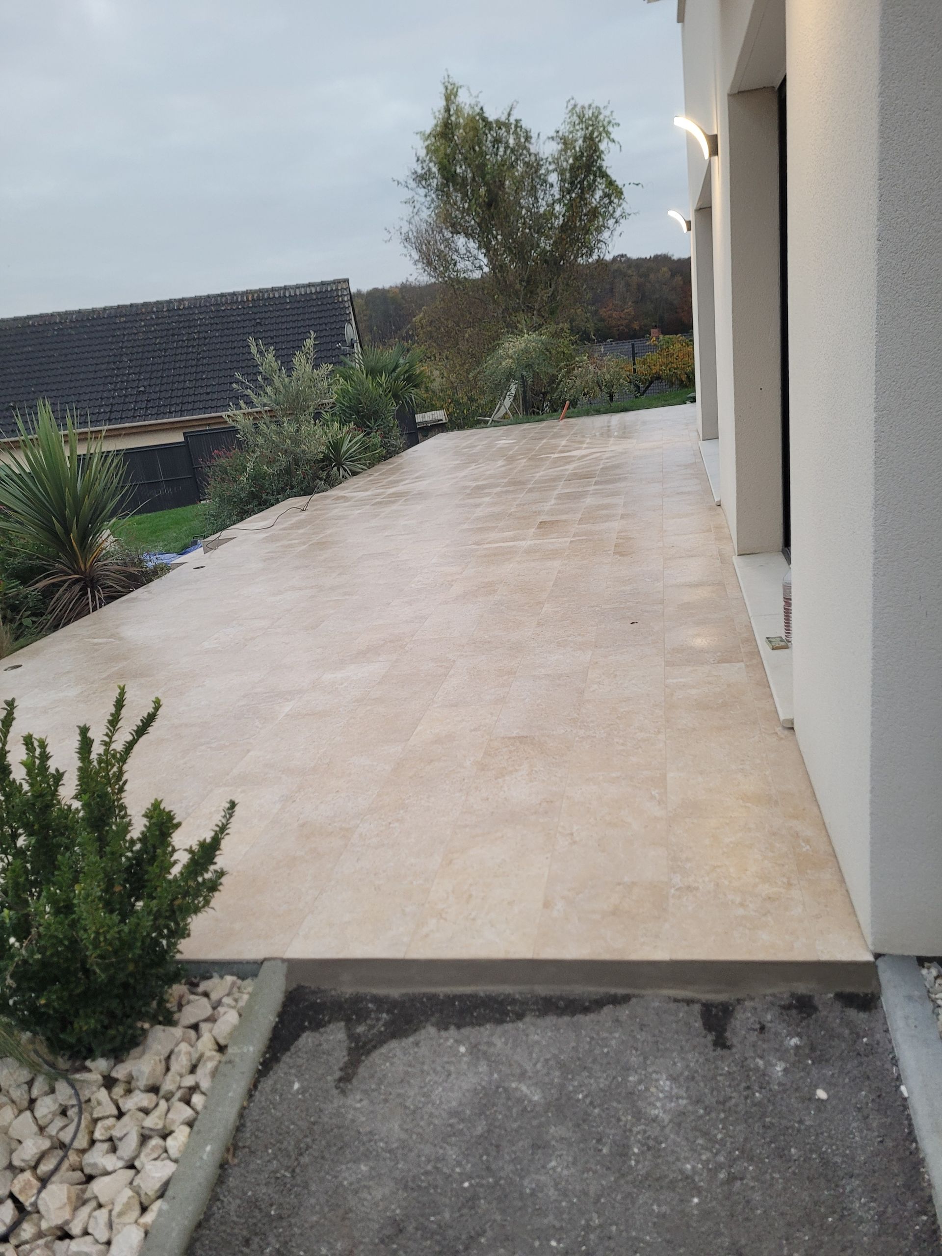 Terrasse dallée claire autour d'une maison individuelle donnant sur un jardin