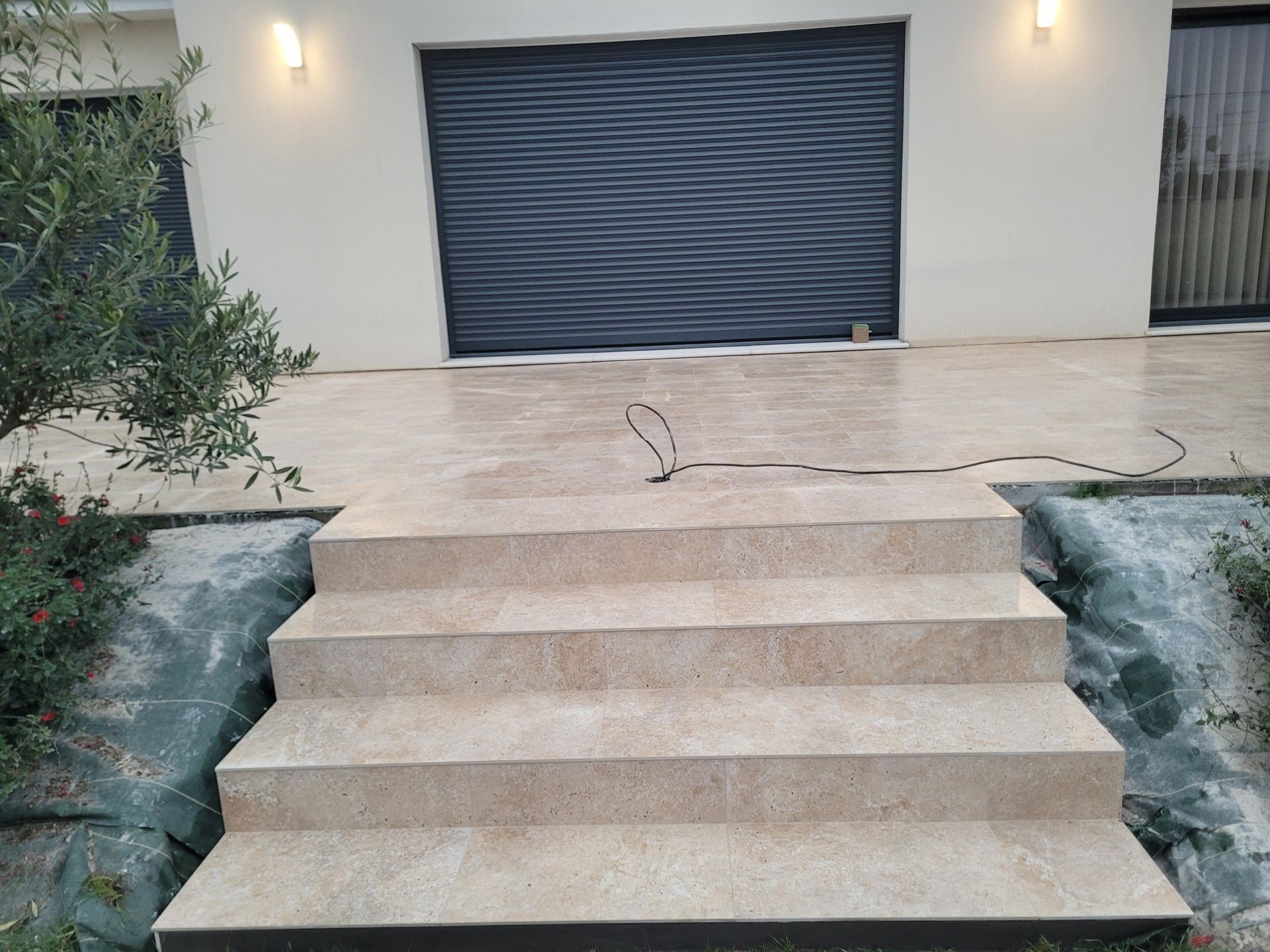 Escalier extérieur dallé donnant sur une terrasse unie et une porte de garage sombre