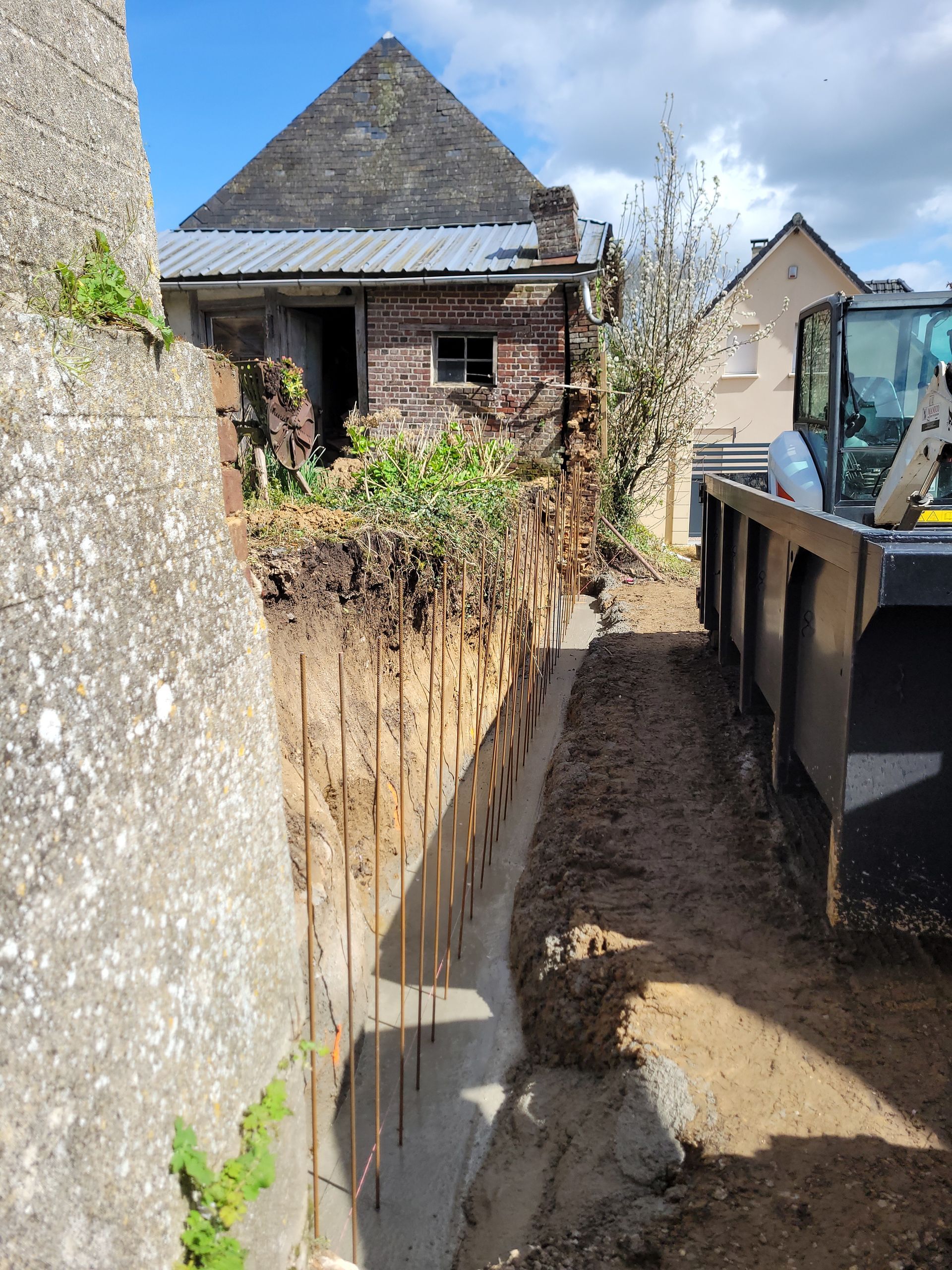Mur en cours de rénovation de maçonnerie avec à gauche une benne facilitant les travaux