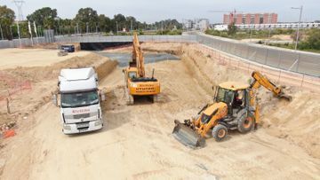 Obra en construcción con camión y dos excavadoras en una zanja de excavación arenosa.
