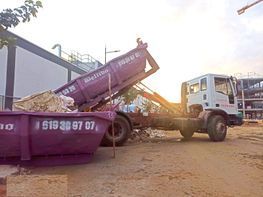Un camión volquete morado volcado en un arcén polvoriento, con un camión blanco al lado, al atardecer.