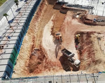 Obra en construcción con excavadora y camión volquete excavando tierra junto a los cimientos de un edificio.