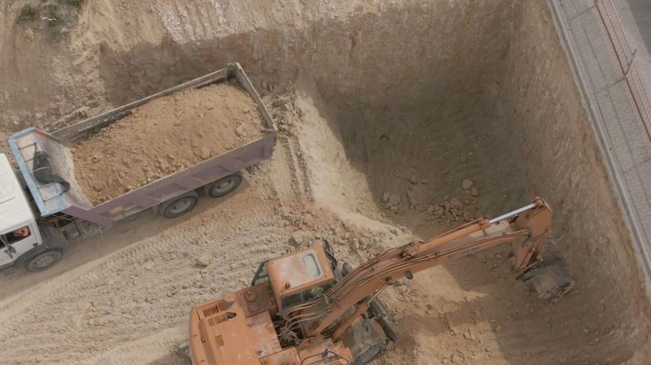 Camión volquete y excavadora cargando tierra dentro de una zanja de construcción vista desde arriba