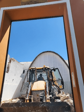 Excavadora trabajando dentro de la estructura de un edificio bajo un cielo azul despejado.
