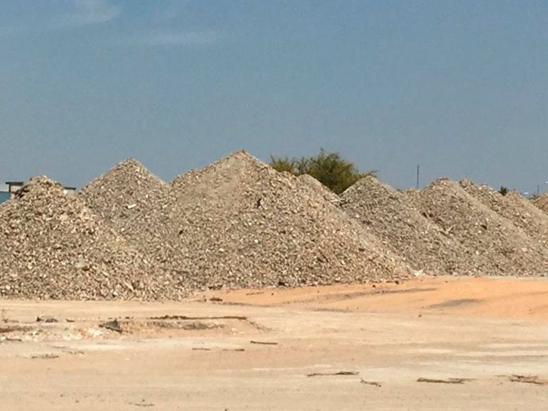 Montones de grava gris en un terreno arenoso de construcción bajo un cielo azul despejado.