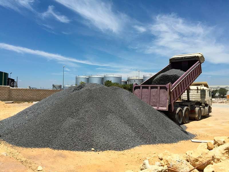 Camión volquete descargando una gran pila de grava en un sitio industrial bajo un cielo azul.